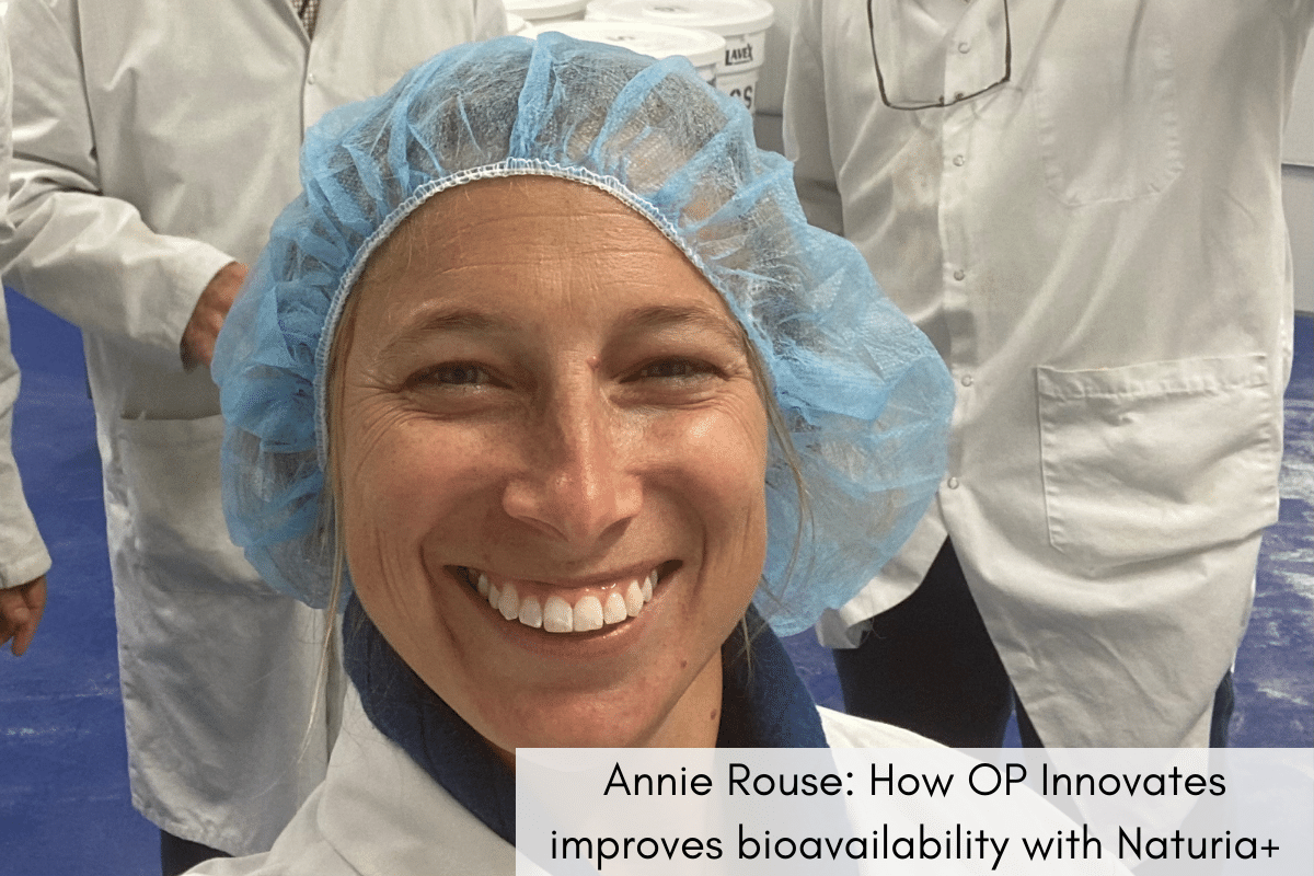 A close up of Annie Rouse in a lab coat and hairnet, smiling in a lab with others in lab coats behind her. In a text book are the words, "Annie Rouse: How OP Innovates improves bioavailability with Naturia+".